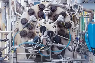 Close-up of a large industrial compressor with multiple piping connections, valves, and instrumentation used in a processing facility.