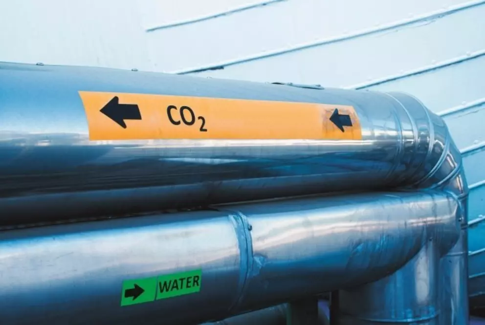 Industrial metal pipelines labeled for CO₂ and water flow, indicating directional transport.